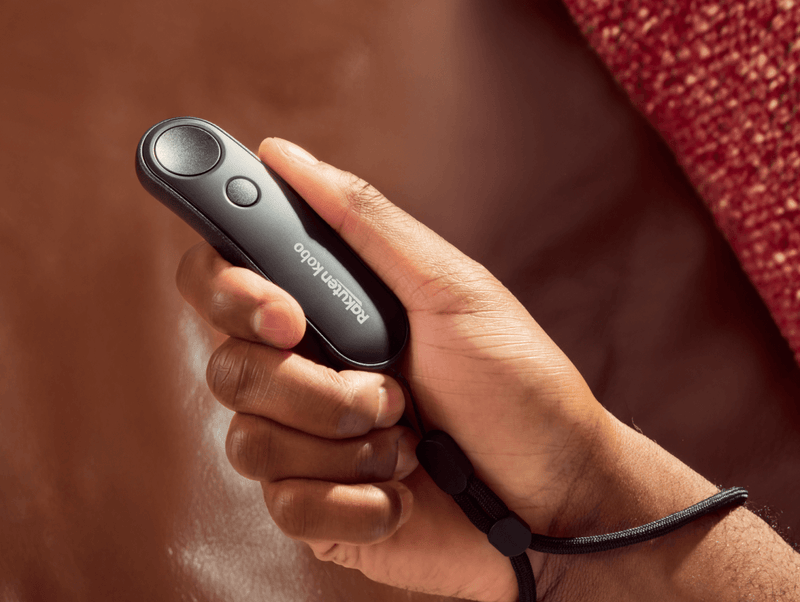 A black Kobo Remote is shown in someone's right hand, with the lanyard at the base of the remote wrapped around their wrist.